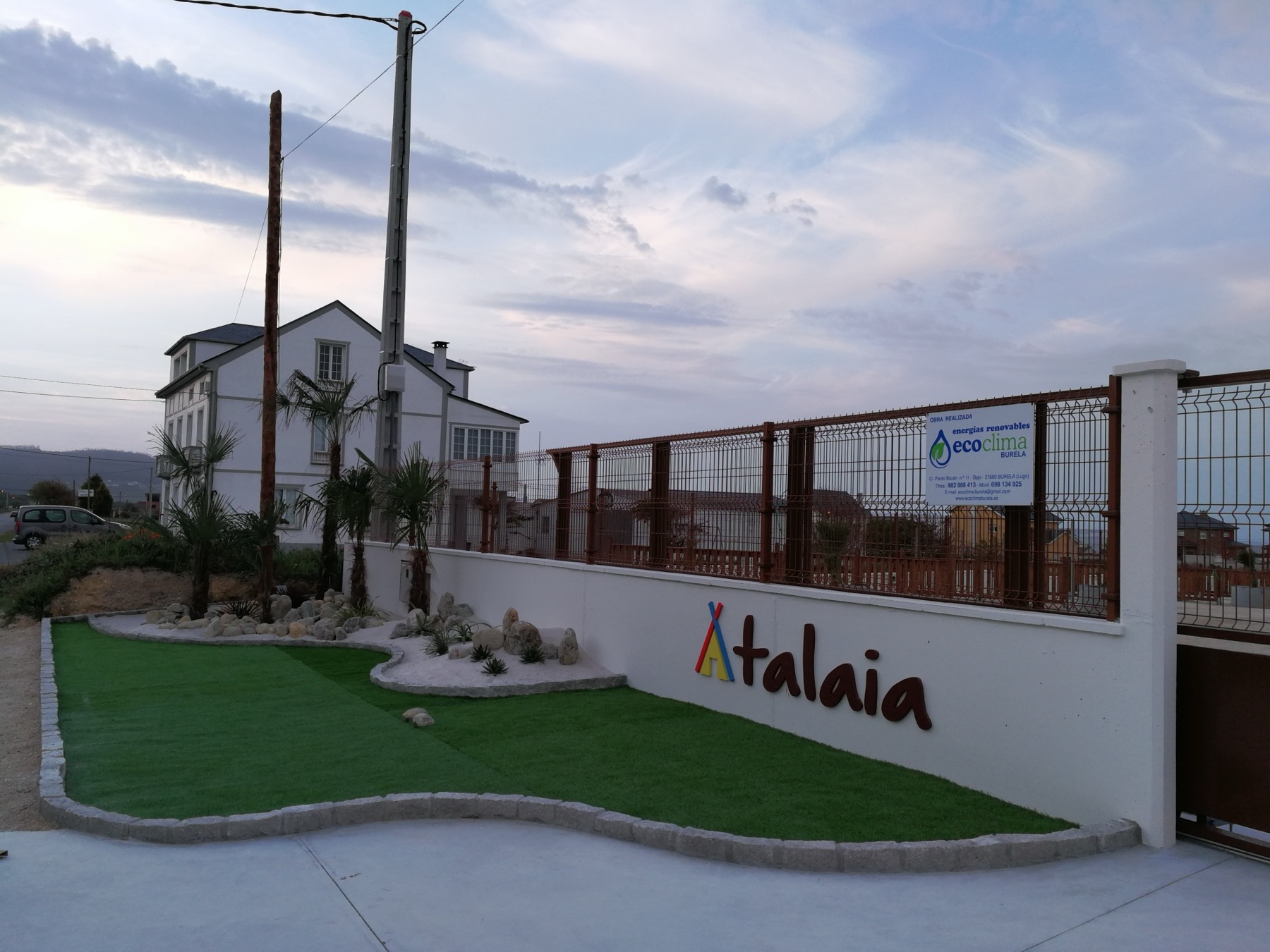 Entrada de Atalaia Camper Park al atardecer, con el rótulo y el jardín de palmeras